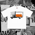 Box Truck Tee — white tee with a black-line box truck against chain-link and an orange graffiti throw-up across the cargo door